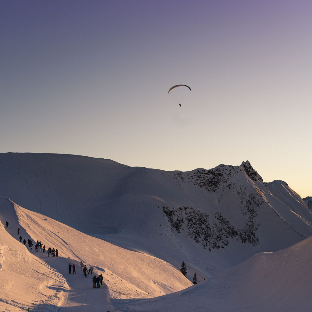 Gleitschirmflieger über dem verschneiten Nebelhorn bei Sonnenuntergang.